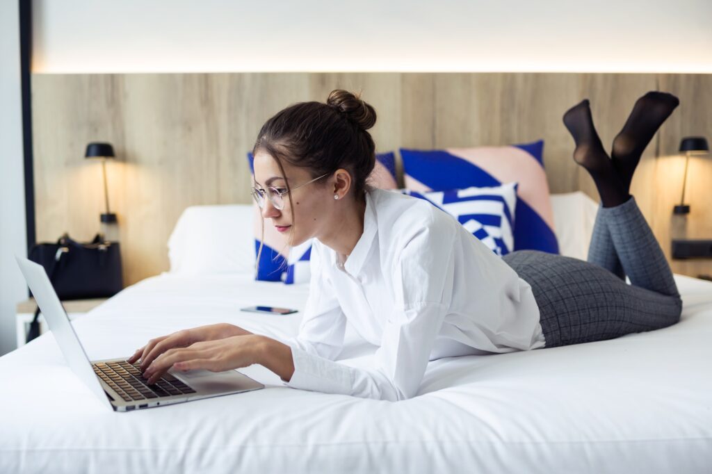 Smart young businesswoman working with her laptop lying on bed i